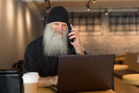 Mature Bearded Hipster Man Using Phone And Laptop Inside The Coffee