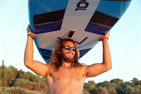 Shirtless Man Carrying Paddleboard On Head At Beach During Sunset Stock