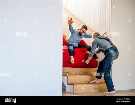 An Adult Hipster Son And Senior Father Sliding On Stairs Indoors At