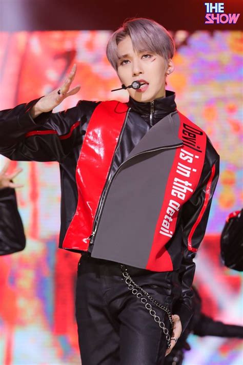 A Male In A Black And Red Jacket Is Standing On Stage With His Hands Out