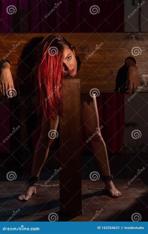 A Redhead Woman Is Imprisoned In A Wooden Pillory During Sex Games