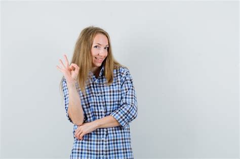 Blonde Frau im Hemd zeigt ok Geste und sieht fröhlich aus Kostenlose Foto