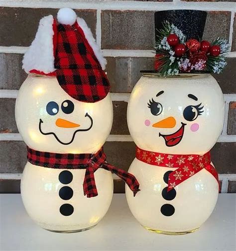 Two Lighted Snowmen Standing Next To Each Other On A White Table With