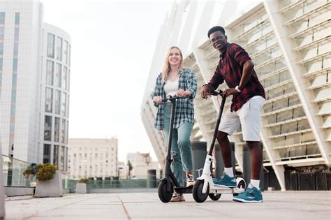 Premium Photo Multiracial Couple Riding Electric Scooters In The City Afro American Guy And