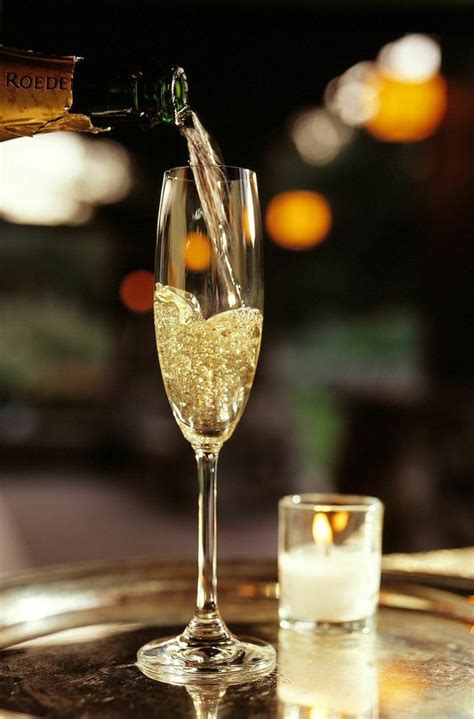 Champagne Being Poured Into A Wine Glass On Top Of A Table With A Lit