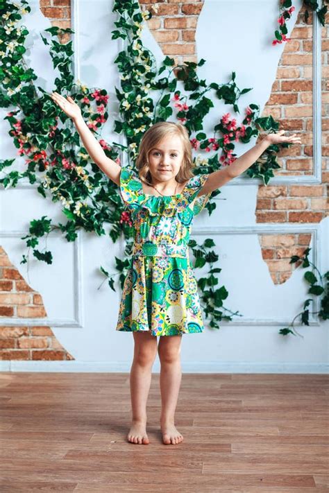 Une Petite Fille Blonde Dans Une Robe Lumineuse a Soulevé Ses Bras Dans Une Chambre Décorée Des