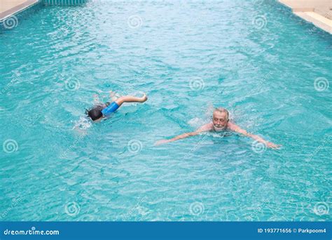 Happy Elderly Caucasian Husband And Elderly Asian Wife Swimming In Pool During Retirement