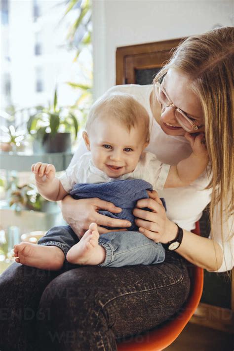 Portrait Of Smiling Baby Boy Sitting On Lap Of His Mother Stock Photo