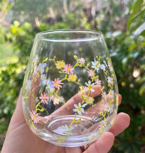 A Hand Holding Up A Wine Glass With Flowers Painted On The Outside And