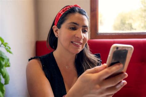 Mujer latina joven que mira el dispositivo móvil en un retrato del restaurante o del pub Foto