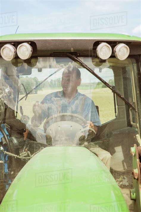 Smiling Farmer Driving Tractor At Farm On Sunny Day Stock Photo