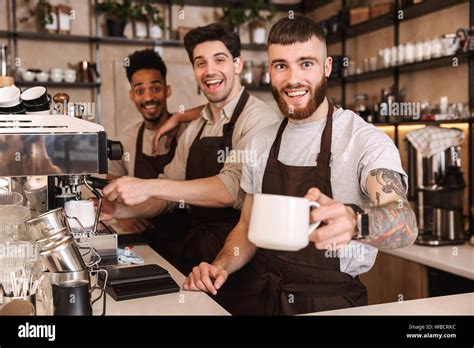 Three Cheerful Male Baristas Standing At The Coffee Shop Counter