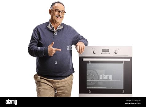 Smiling Mature Man Leaning On An Oven And Pointing Isolated On White