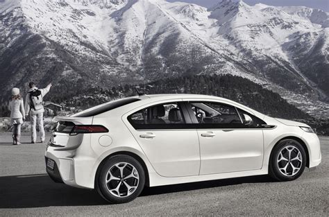 A White Car Is Parked In Front Of Some Mountains With People Looking At