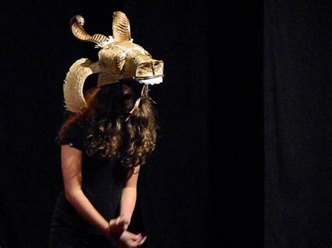 A Woman Standing In Front Of A Black Background Wearing A Gold Mask