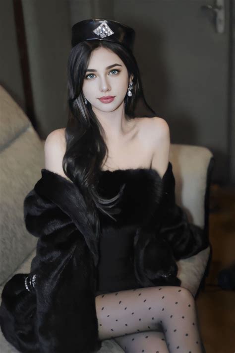 A Woman Sitting On Top Of A Couch Wearing A Black Dress And Fur Stoler