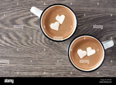 Two Cups Of Hot Chocolate With Heart Shaped Marshmallows Over A Wooden
