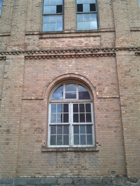 An Old Brick Building With Two Windows And A Clock On The Front Window Sill