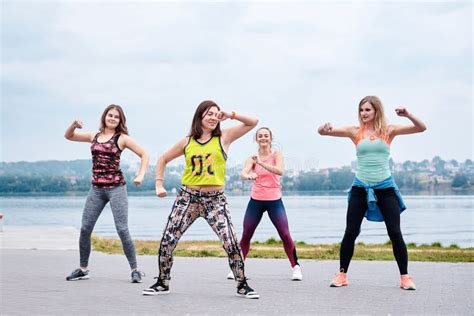 A Group of Young Women, Wearing Colorful Sports Outfits, Doing Zumba Exercises Outside by City ...