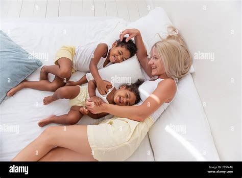 Une jeune mère blonde caucasienne joue se trouve sur un lit blanc avec une fille afro