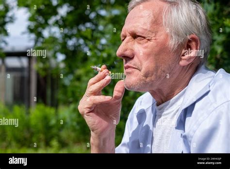 Old Man Smoking A Cigarette In A Sunlit Park Candid Shot Suitable For