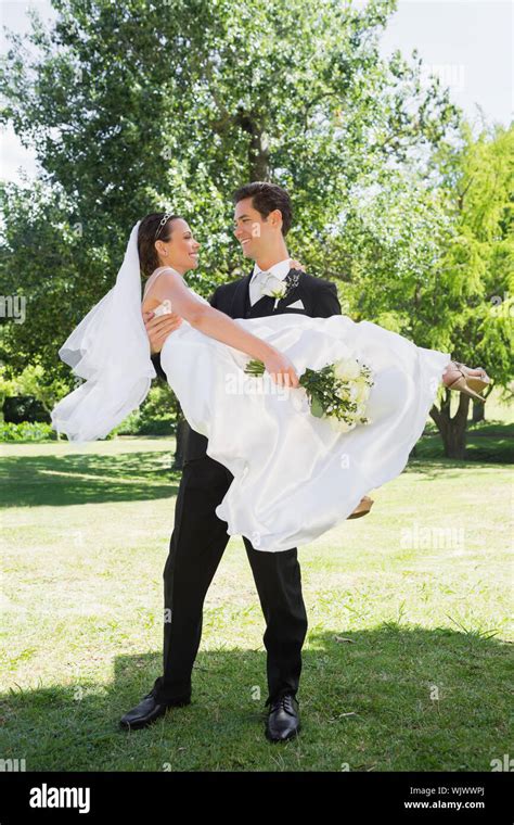 Full Length Of Happy Groom Carrying Bride In Arms At Garden Stock Photo