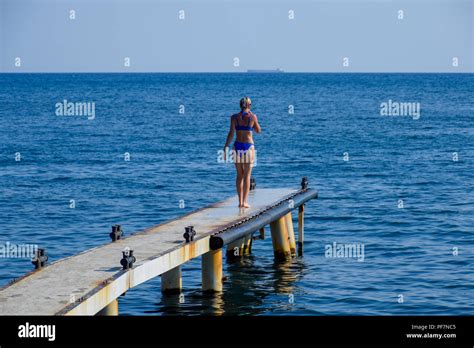 Ein schönes Mädchen in einem blauen Bikini geht den Pier zum Meer Marine Betonpfeiler Ins