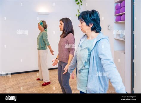 Side View Of Three Mature Adult Women With Arms Opened Breathing During Qi Gong Class Indoors