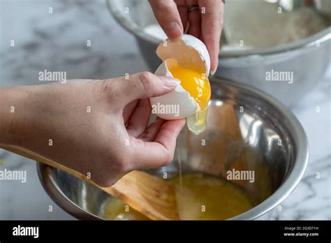 Womans Hand Cracking An Egg Open With The Yellow Yolk Over A Round