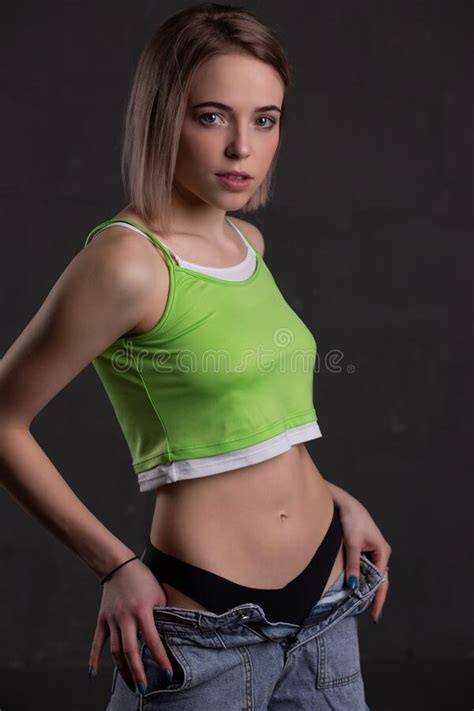 Gorgeous Blonde Girl In A Crop Top And Jeans Poses On A Dark Background
