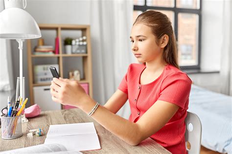 Girl With Smartphone Distracting From Homework Stock Photo Download