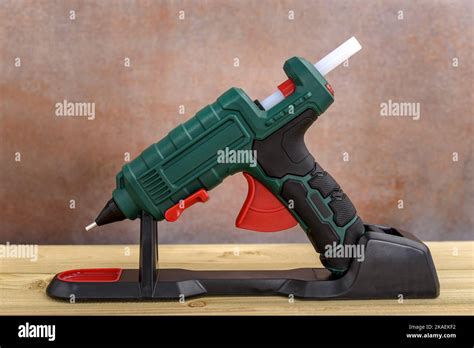 Electric Hot Glue Gun With Stand And White Glue Sticks On Wooden Background Selective Fokus