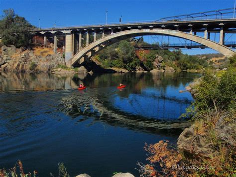 Two Kayakers Paddling Under A Bridge Over A River