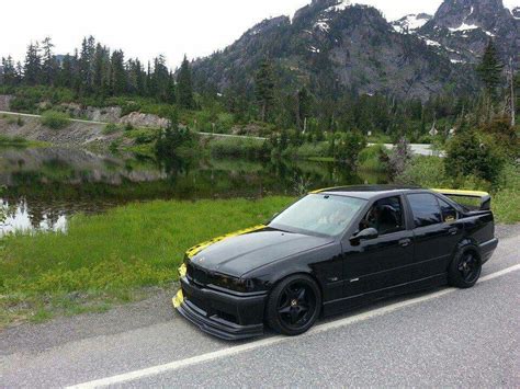 A Black Car Parked On The Side Of A Road Next To A Lake And Mountains