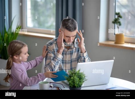 Tired Dad Sitting At Laptop Covering His Eyes And Daughter Stock Photo