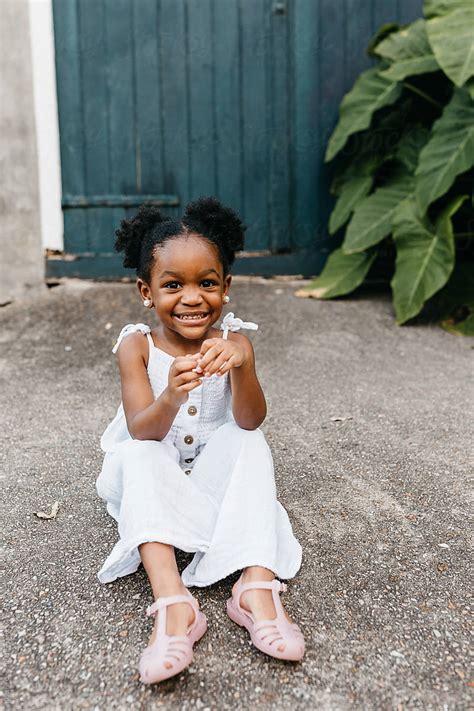 An Adorable African American Girl Outside In A Cute White Dress Sitting On The Concrete By