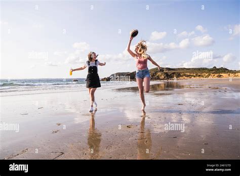 Two Girlfriends Having Fun Running And Jumping On The Beach Stock