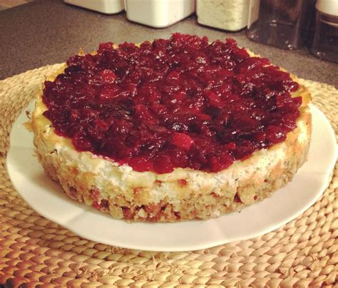 A Cheesecake Covered In Cranberry Sauce Sitting On A Plate Next To Jars