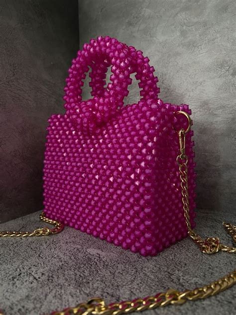 a pink handbag sitting on top of a cement floor next to a gold chain