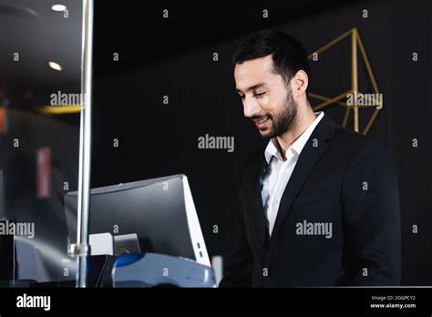 Smiling Receptionist Working Near Computer Monitor In Hotel Stock Photo