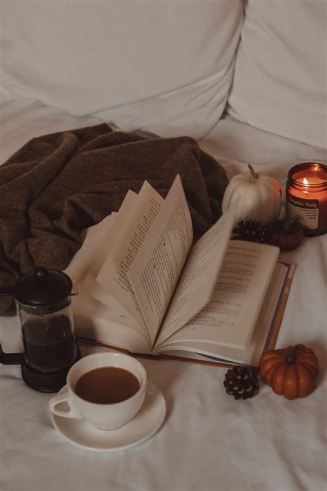 An Open Book And Cup Of Coffee Sit On A Bed Next To A Blanket Candle