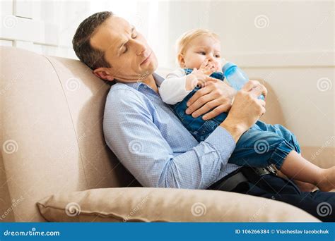 Tired Father Falling Asleep While Sitting With His Active Baby Stock