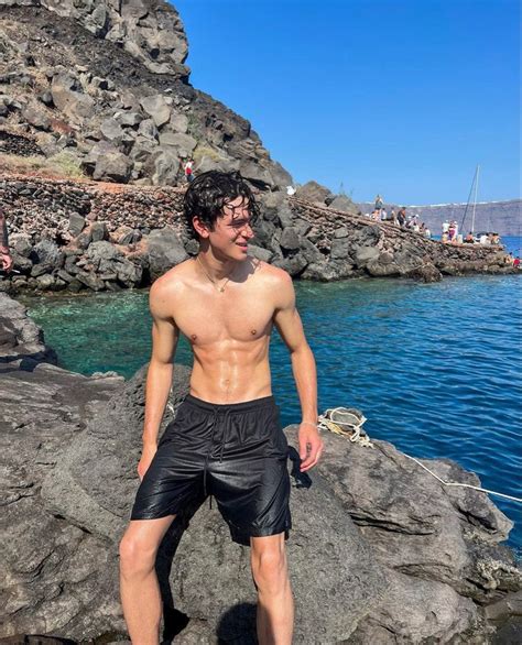 A Man Standing On Top Of A Rock Next To The Ocean With His Shirt Off