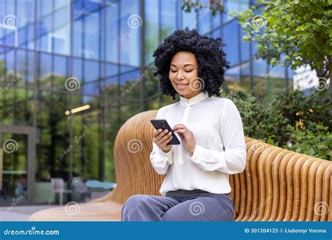 A Young African American Business Woman Is Sitting Outside On A Bench