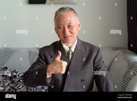 Happy Mature Japanese Businessman Smiling And Giving Thumbs Up At Home