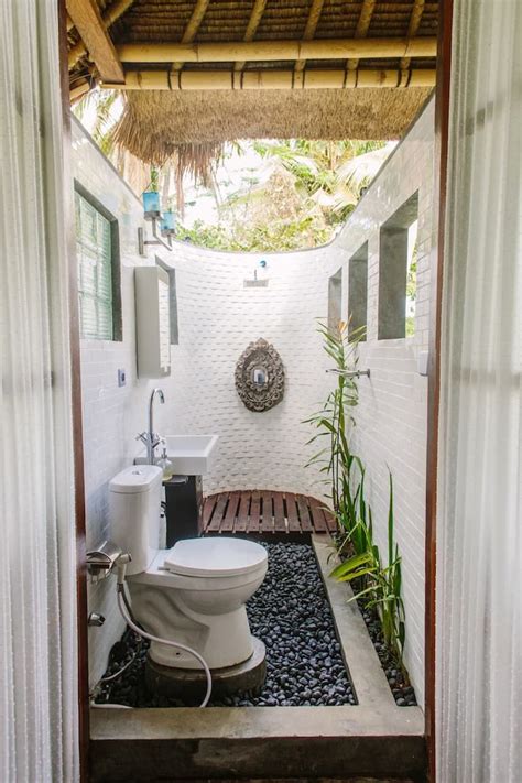 A White Toilet Sitting Inside Of A Bathroom Next To A Bamboo Roof Over