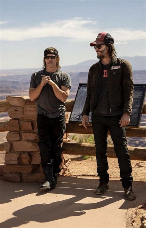 two men standing next to each other in front of a sign on a mountain top