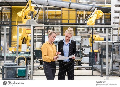 Zwei Frauen im Gespräch in der Fabrikhalle mit Industrieroboter ein