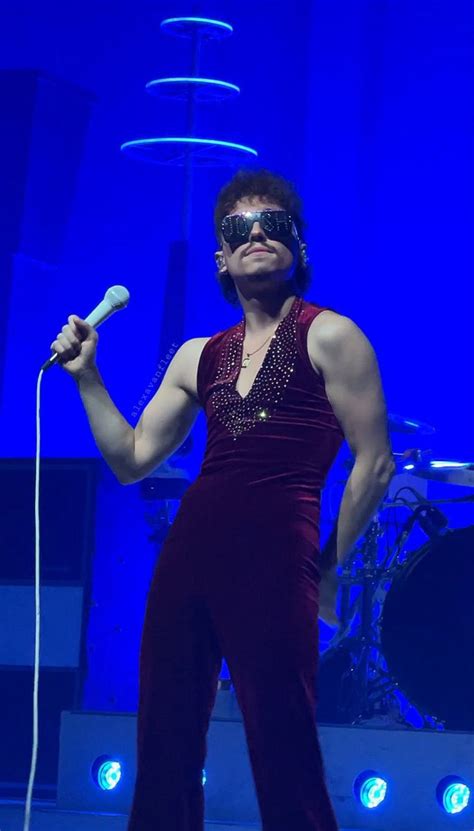 A Man In A Red Outfit Holding A Microphone And Wearing Blindfolds On Stage