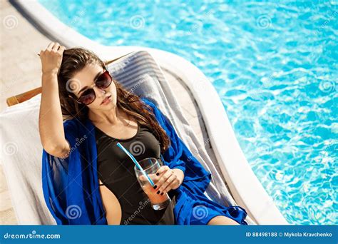 Beautiful Girl Drinking Cocktail Lying On Chaise Near Swimming Pool